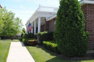 A building with American flags and neatly trimmed greenery on a sunny day.
