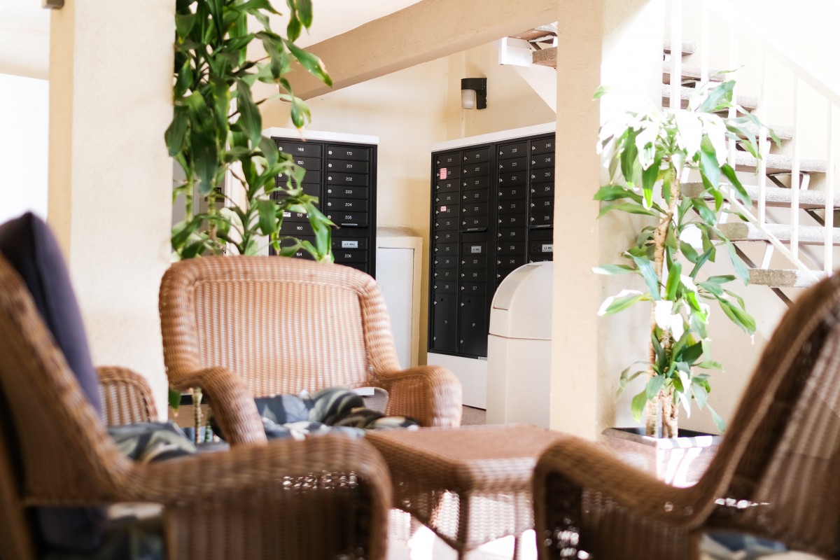A cozy lobby area with wicker chairs, plants, and mailboxes in the background.