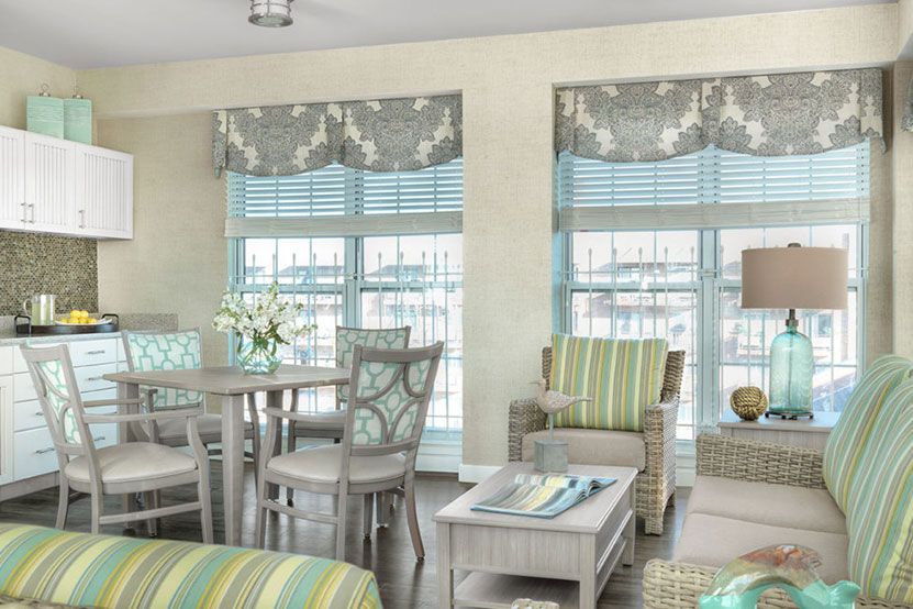 A bright and airy living room featuring pastel-colored furniture and large windows with patterned curtains.