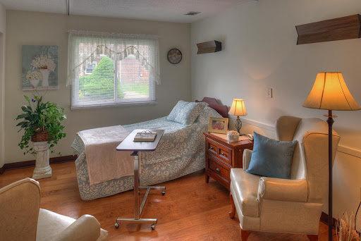 A cozy and well-lit hospital room featuring a bed, armchair, and side table.