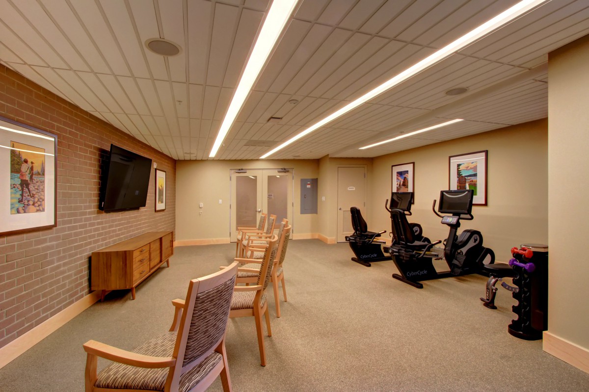 A cozy indoor fitness room with exercise equipment and chairs facing a television.