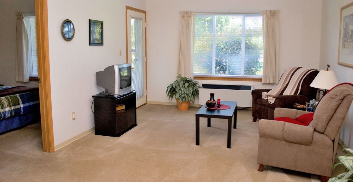 A cozy living room with a television, coffee table, and large window.