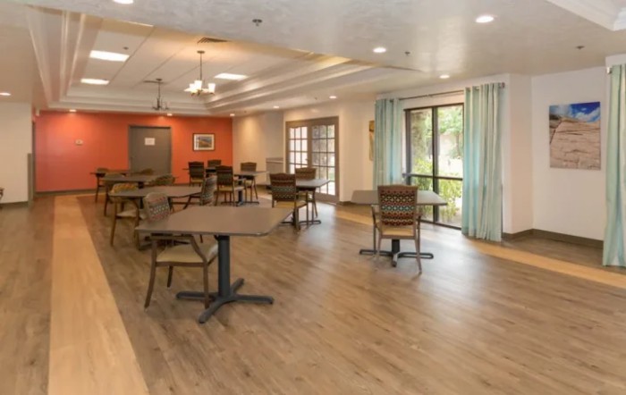 A spacious dining room with wooden tables and chairs, featuring large windows allowing natural light to fill the space.