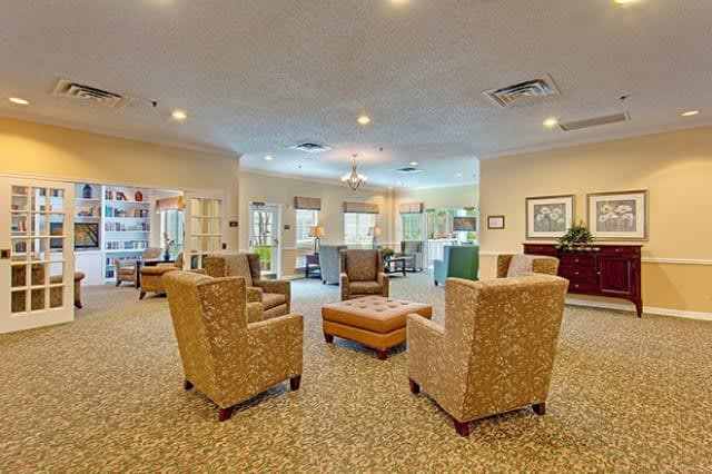 A spacious and cozy living room with armchairs arranged around an ottoman on a carpeted floor.