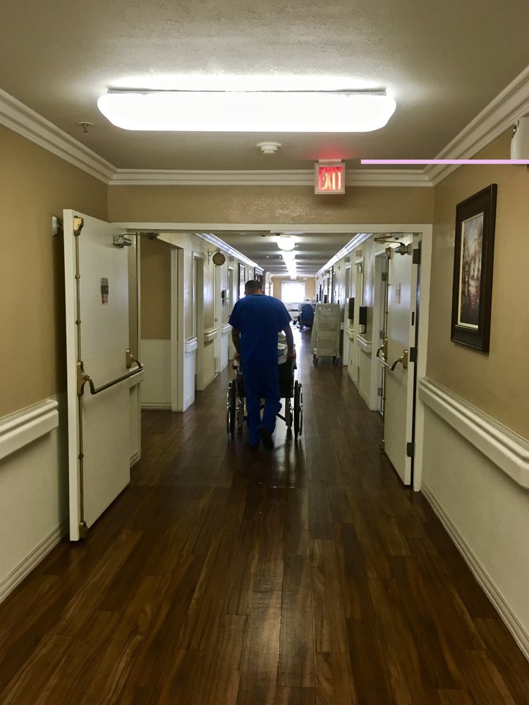 A healthcare professional pushes a wheelchair down a hospital corridor.