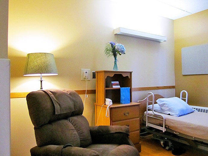 A cozy hospital room with a bed and recliner, featuring a lamp and a small shelf.