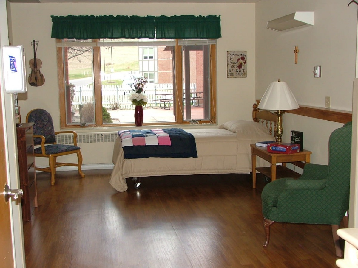 A well-lit bedroom with a bed, chairs, and a large window letting in natural light.