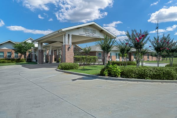 A beautifully landscaped building entrance with a covered driveway under a blue sky.