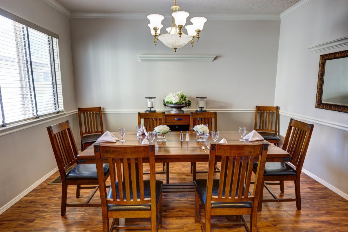 A well-appointed dining room with a wooden table set for a meal, surrounded by matching chairs and illuminated by an elegant chandelier.