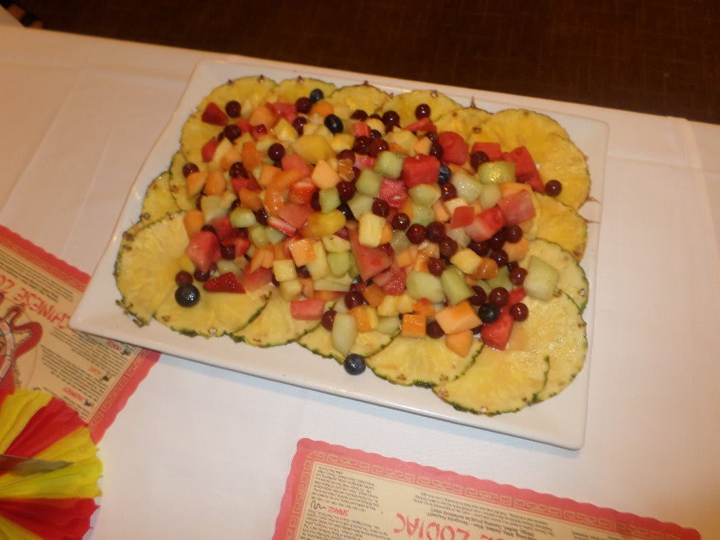 A colorful fruit platter featuring sliced pineapples and an assortment of mixed fruits and berries, displayed at a buffet table.