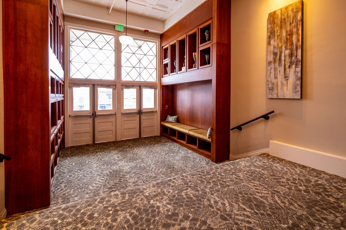 A warmly lit hallway with patterned carpet, wood paneling, and large windows.