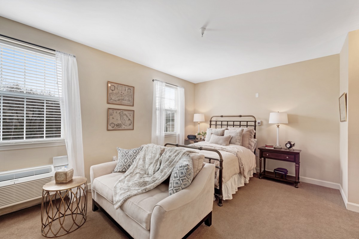 A cozy bedroom with neutral tones, featuring a bed, sofa, and elegant decor.