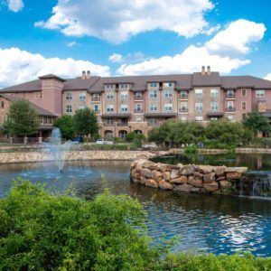 A scenic view of a resort hotel with a beautiful lake and fountain in the foreground.