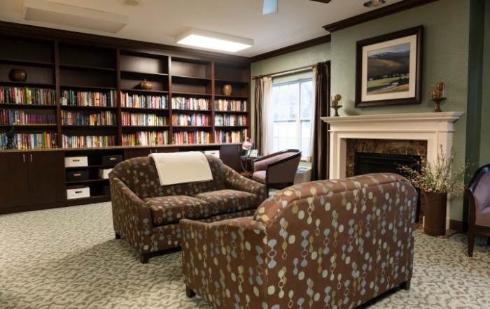 A cozy library with bookshelves, sofas, and a fireplace, creating an inviting reading area.