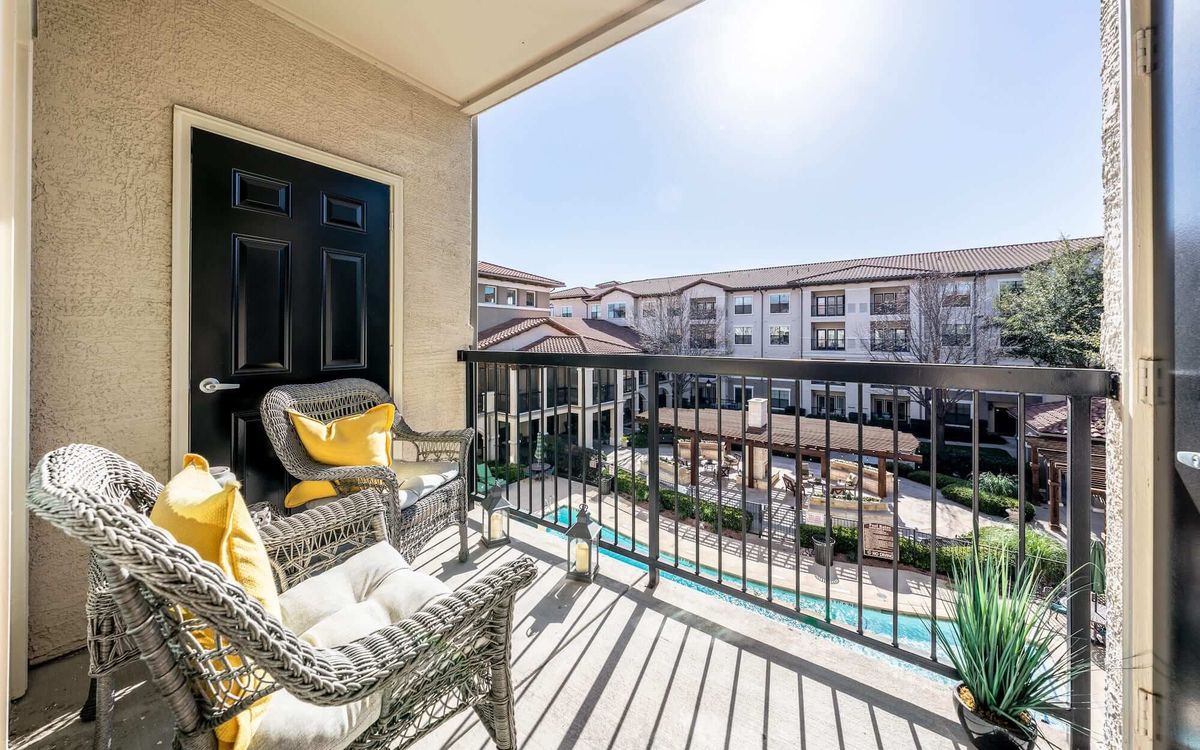 A cozy balcony with wicker chairs overlooking a pool in an apartment complex on a sunny day.