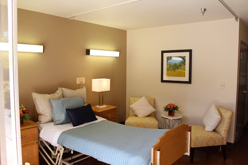 A well-lit hospital room featuring a twin bed, cozy seating, and decorative art.