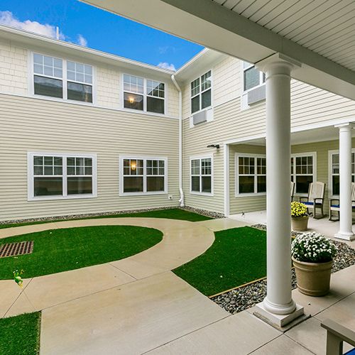 A well-maintained courtyard with a pathway, surrounded by a two-story building and featuring white columns.