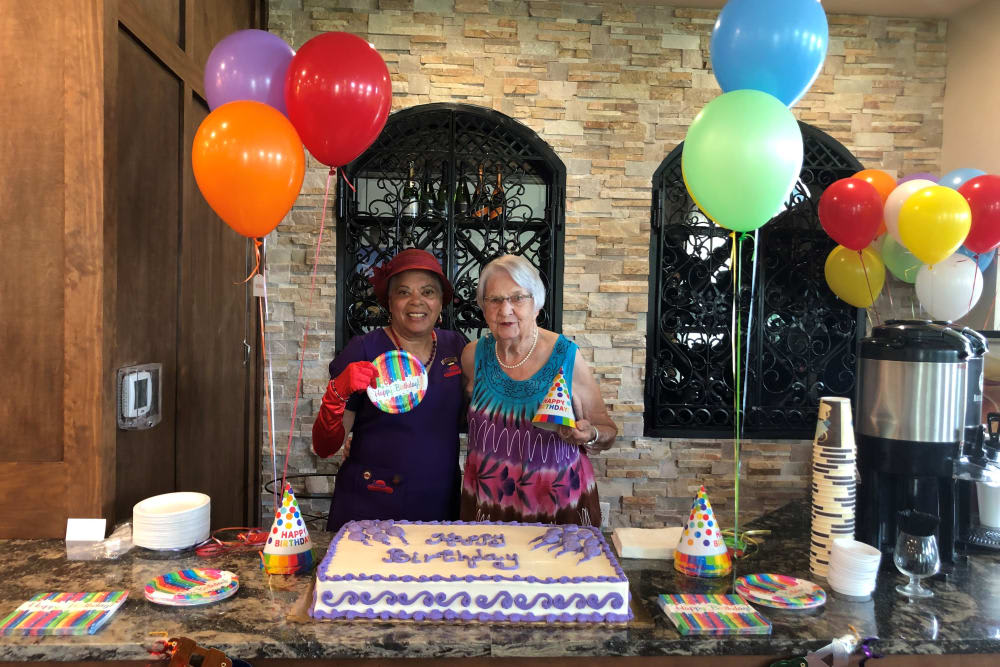 Two people celebrating a birthday with a cake and colorful balloons.