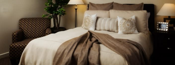A cozy bedroom setting with neatly arranged pillows, a soft blanket, and a warm lamp.