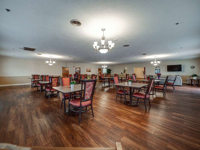 A spacious dining room with wooden floors, featuring tables and chairs under elegant chandeliers.