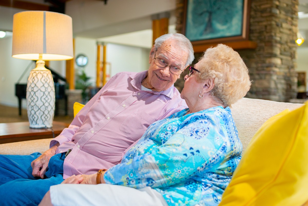 An elderly couple sitting together on a couch, sharing a joyful moment.