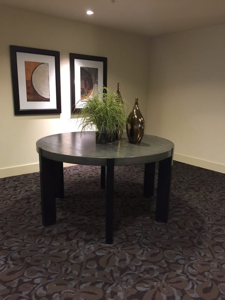A round table with decorative vases and a plant, set in an indoor carpeted area adorned with framed artwork on the wall.
