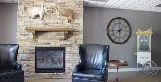 A cozy living room corner with a stone fireplace, leather armchair, and wall-mounted clock.