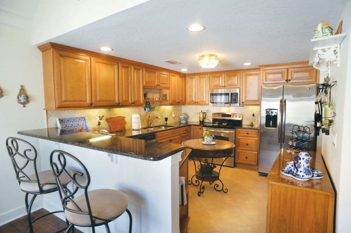 A modern kitchen featuring wooden cabinets, stainless steel appliances, and a granite countertop with bar stools.
