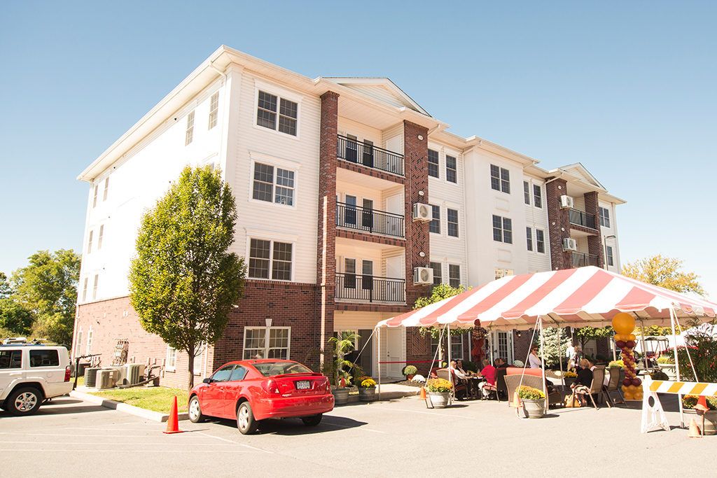 An apartment building with a red car parked in front and a striped tent set up outdoors.