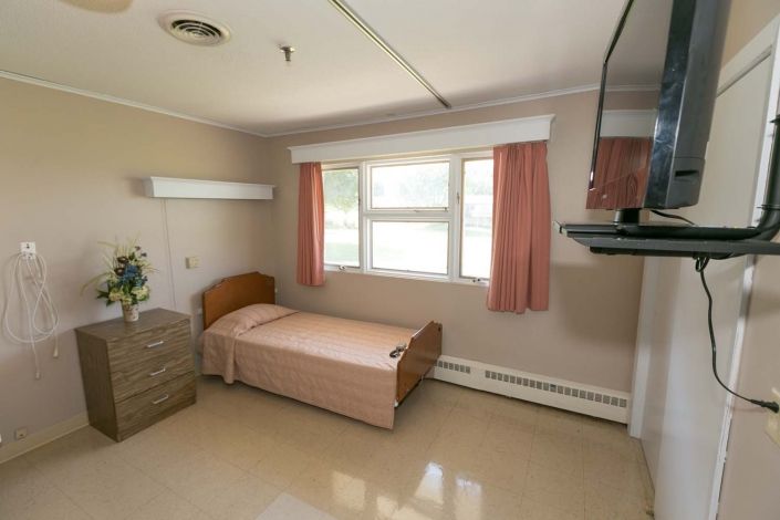 A simple hospital room with a single bed and a window with curtains.