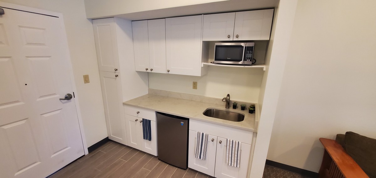 A compact kitchen space with white cabinets, a microwave, a small fridge, and a sink.
