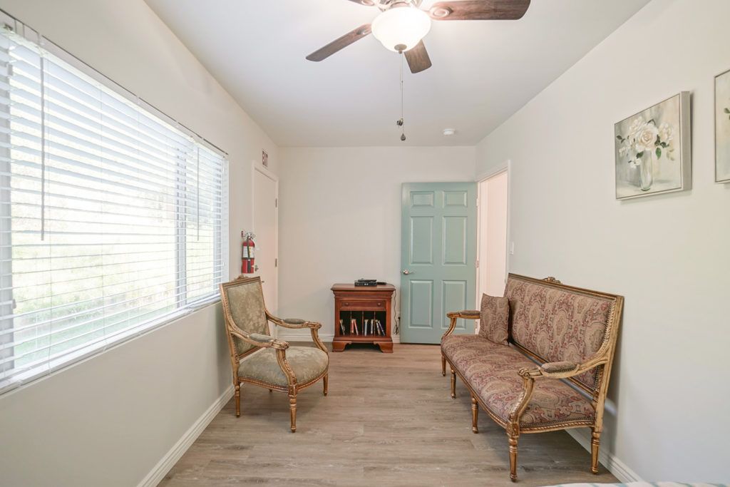 A cozy living room with comfortable seating, a ceiling fan, and natural light from a large window.