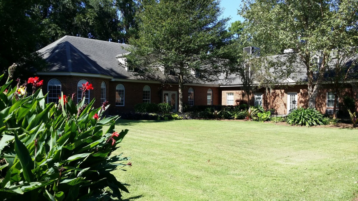A sunny day view of a brick house surrounded by a well-maintained lawn and garden.