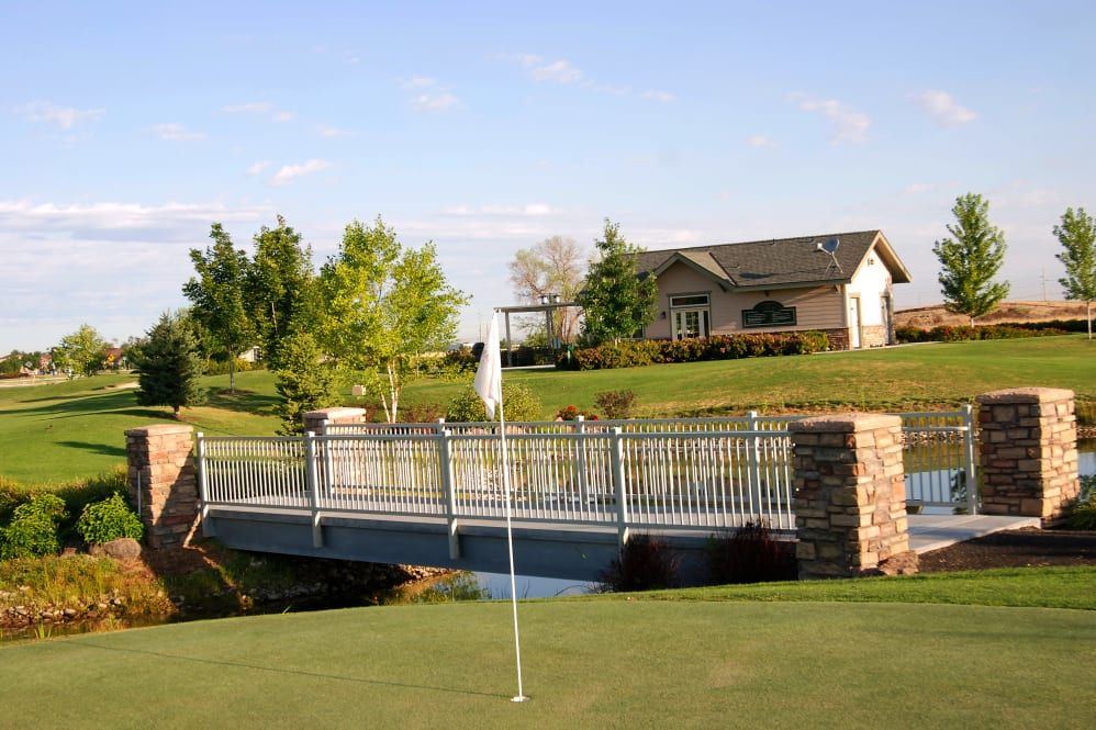 A peaceful golf course featuring a green with a flag, a bridge, and a house in the background.