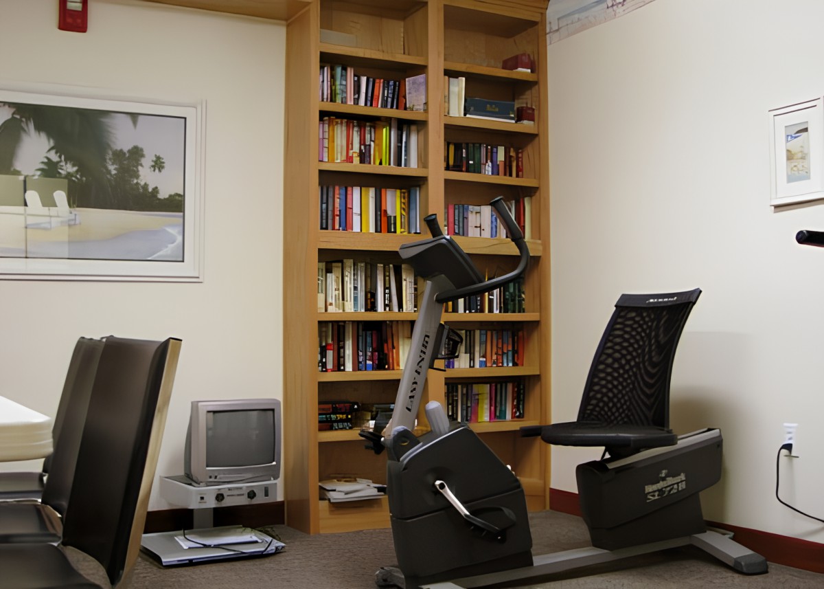 A cozy office space with an exercise bike, bookshelf, and a small TV.