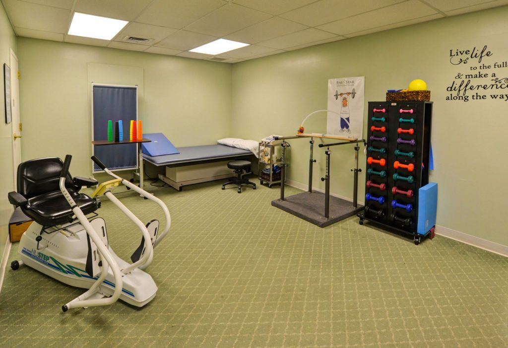 A physical therapy room equipped with exercise equipment, treatment tables, and a weights rack.