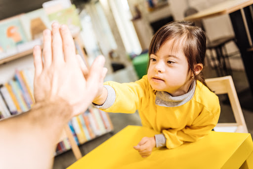 A young child in a yellow shirt reaches out for a high five, engaged in an interactive and playful learning moment.
