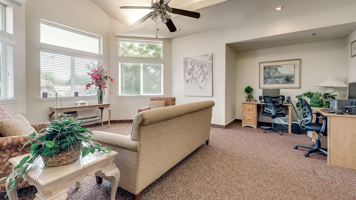 A cozy living room with a couch, large windows, and a ceiling fan.
