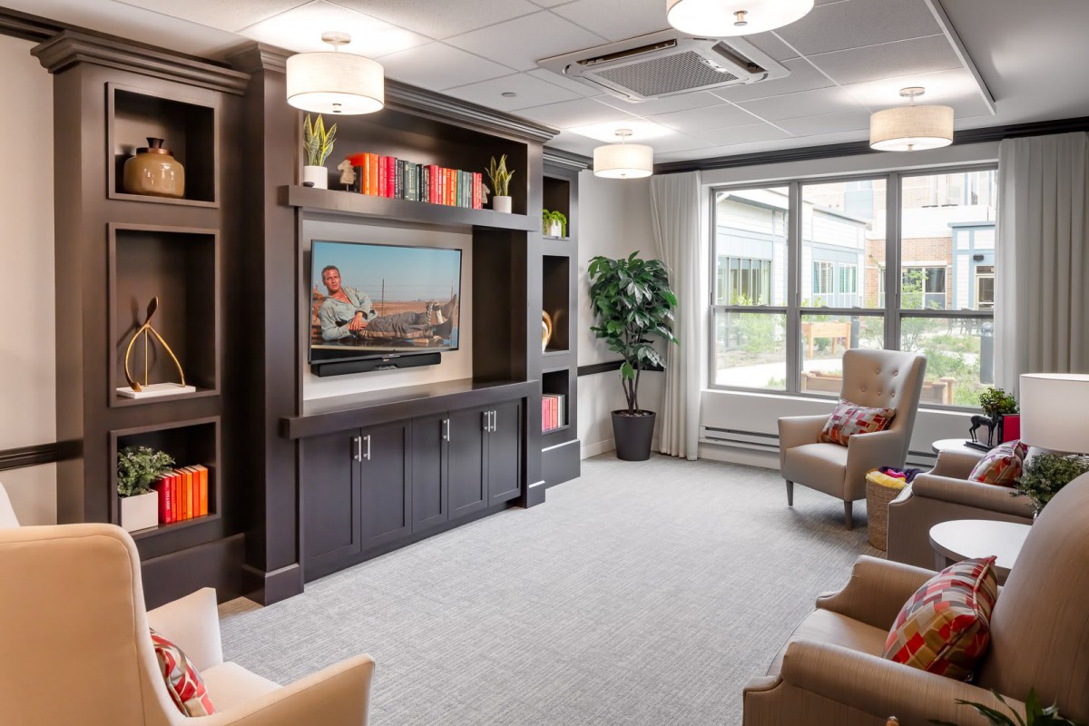 A modern living room with comfortable seating, a large television, and ample natural light from a large window.