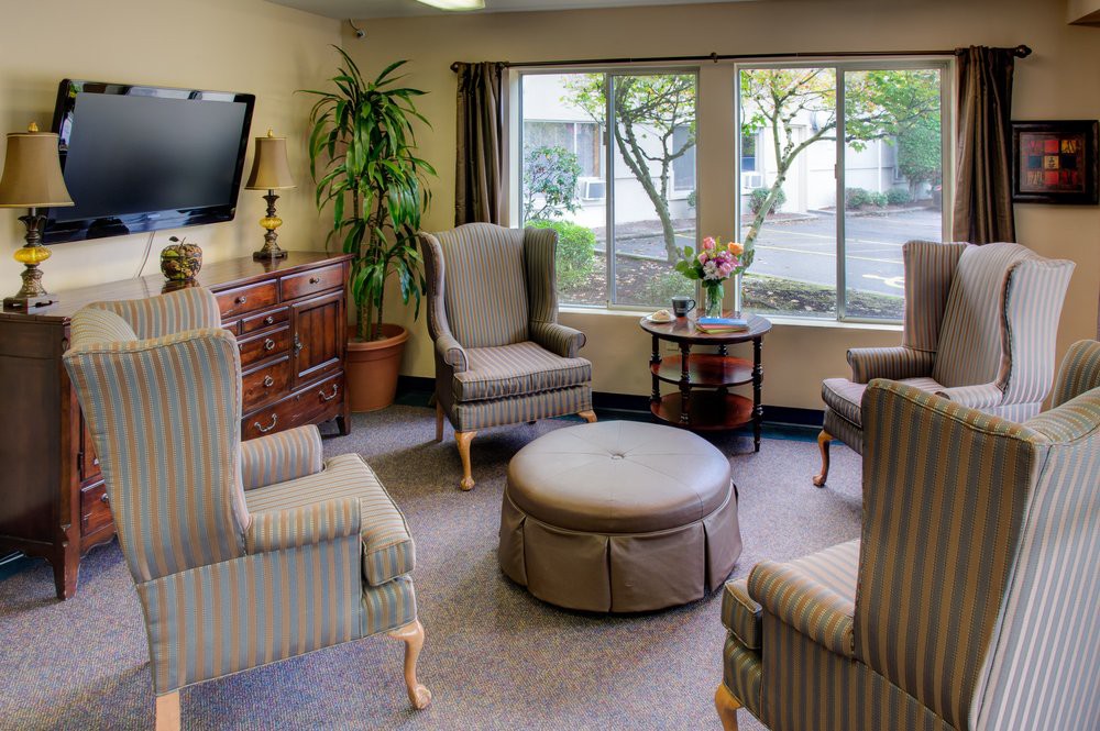 A cozy living room with elegant chairs, an ottoman, television, and a large window allowing natural light in.