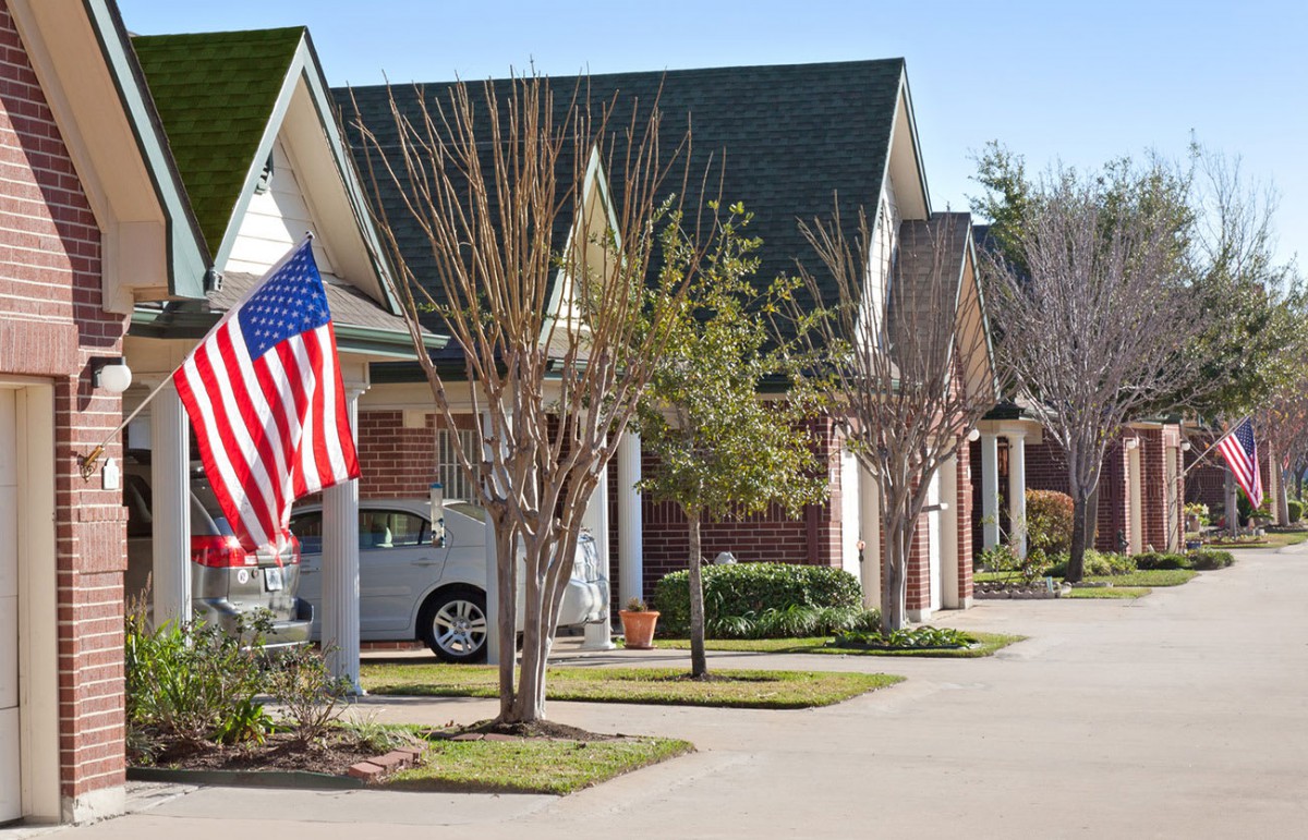 A suburban neighborhood with neatly lined houses and an American flag displayed.