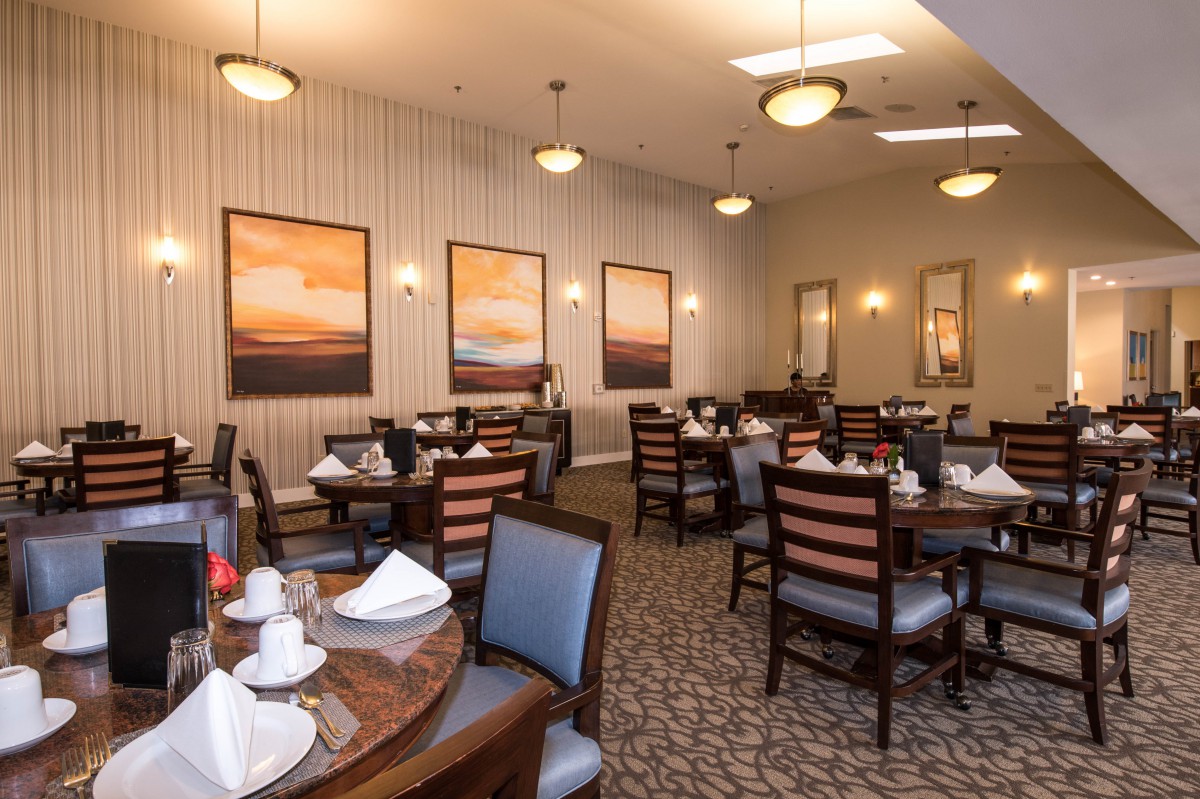 An elegant dining room setup with neatly arranged tables and chairs, decorated with framed artwork on the walls.