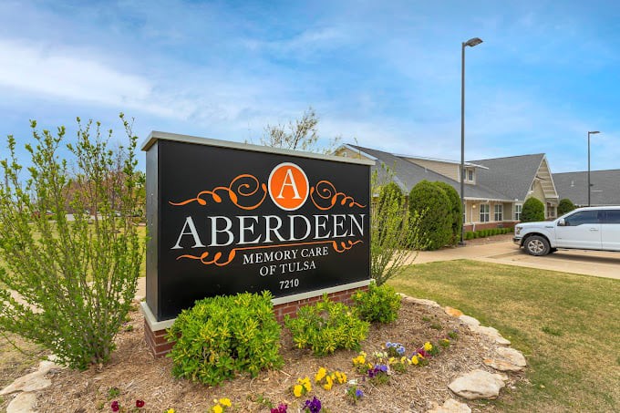 A large sign for 'Aberdeen' in front of a building, surrounded by landscaped greenery and flowers.