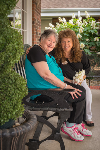 Two women enjoying a joyful moment together on a bench surrounded by flowers.
