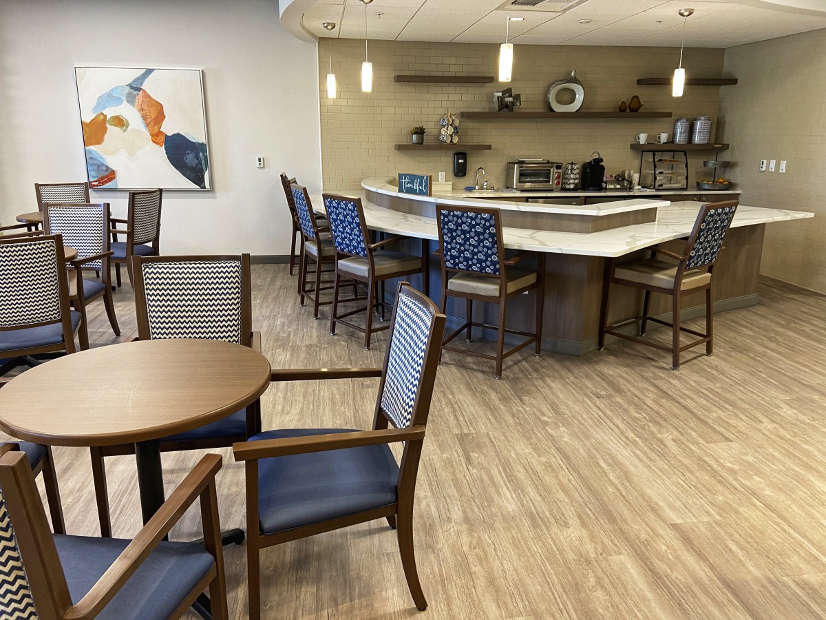 A modern cafe interior featuring a seating area with wooden tables and blue cushioned chairs, alongside a bar counter.