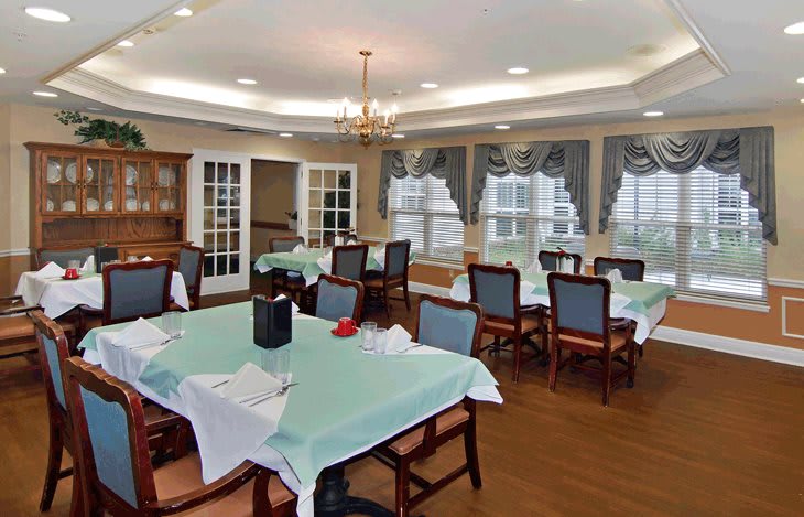 A well-lit dining room with neatly arranged tables and chairs, featuring large windows and elegant decor.