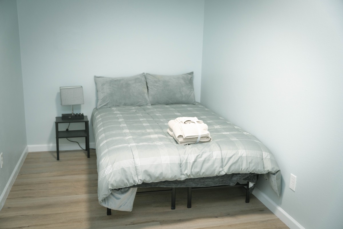 A minimalist bedroom with a neatly made bed and a small nightstand with a lamp.