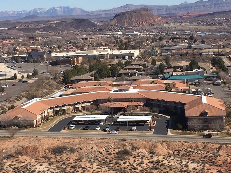 An aerial view of a building complex set in a desert landscape with mountains in the background.