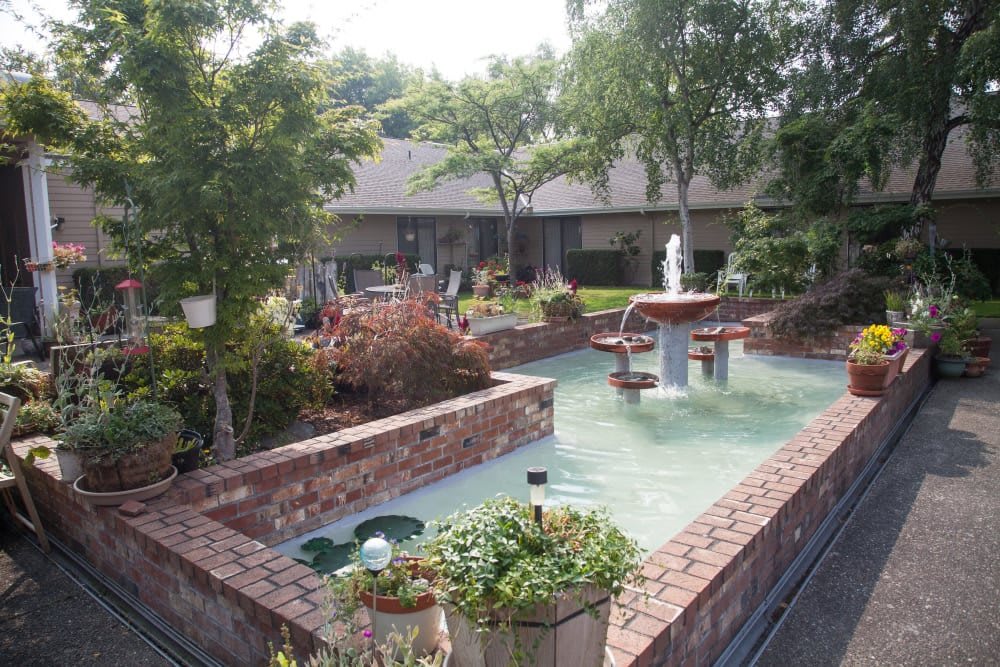 A serene garden courtyard featuring a central fountain surrounded by lush greenery and brick walls.