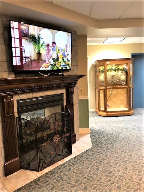 A cozy room featuring a fireplace with a mounted television above, and a decorative display case in the background.